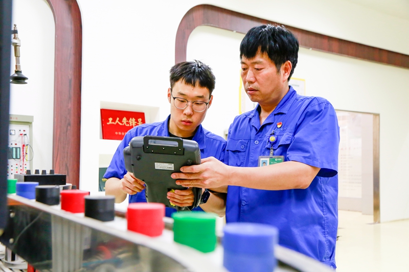 青年维修工正在向师傅请教点检设备使用方法。甘竞摄